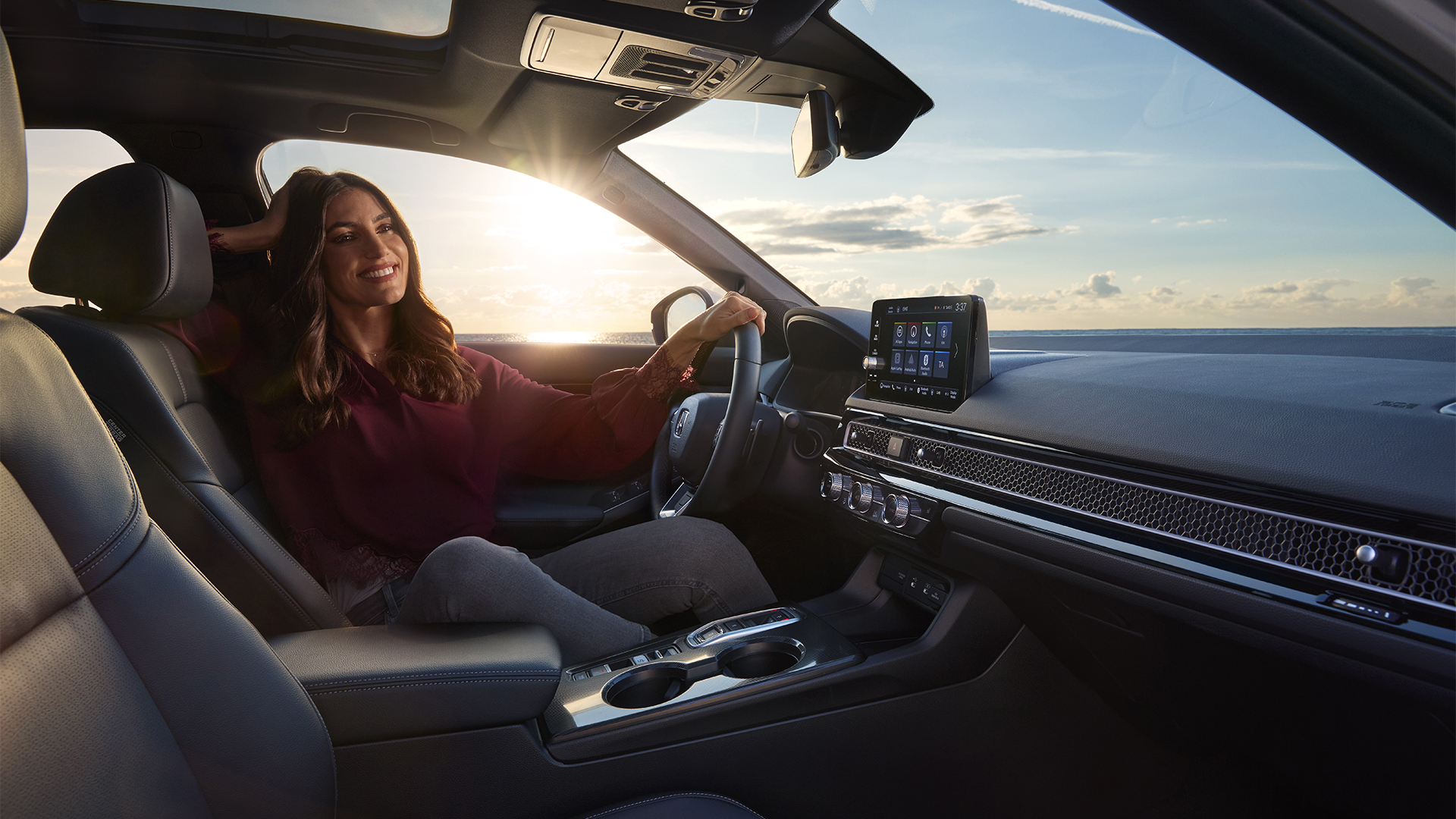 Fotografía tomada desde el interior del Civic Hybrid, una mujer sentada en el coche, junto al mar.