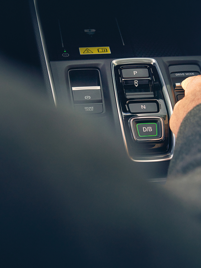 La mano de una persona alcanza para ajustar un interruptor en la consola central de un coche moderno, junto a los botones del selector de marchas.