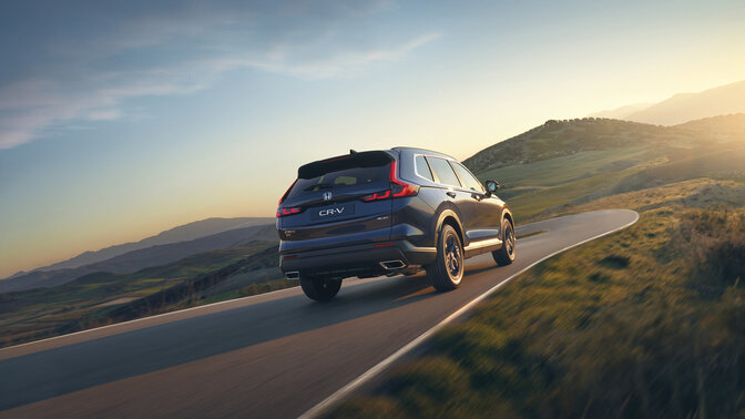 Vista lateral trasera de un SUV CR-V Hybrid azul en una ubicación de montaña.