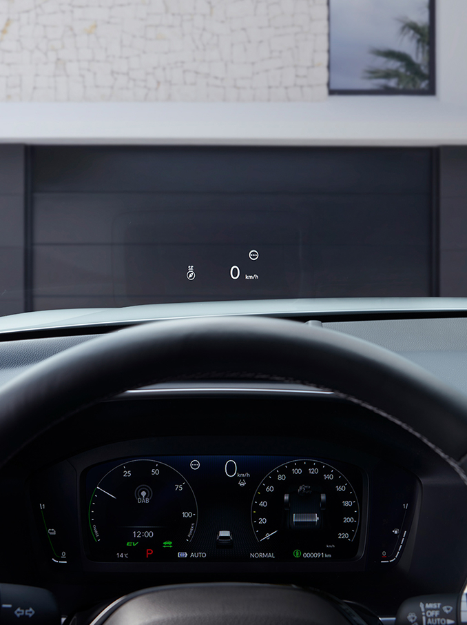 Vista en primera persona desde el asiento del conductor, mostrando un Head Up Display (HUD) que proyecta "50 km/h" y una brújula en el parabrisas sobre un camino de grava.