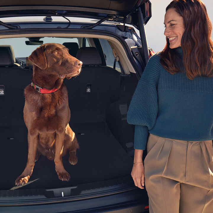 Honda CR-V Híbrido mirando hacia atrás con perro y modelo sentados dentro del maletero.