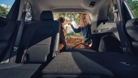 Asiento trasero reclinable del SUV CR-V Híbrido con mujer y perro en el maletero abierto. 