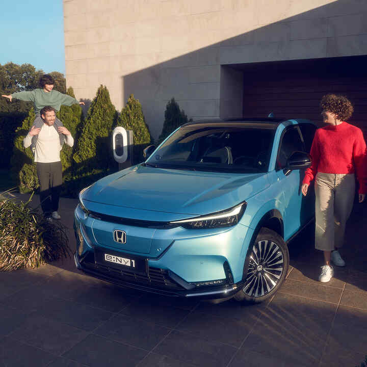 Familia de pie junto al Honda e:Ny1 mirando hacia el frente estacionado delante de casa.