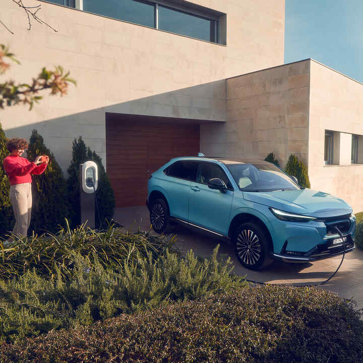 Familia jugando en la entrada junto al Honda e:Ny1 cargando a la puerta de casa.