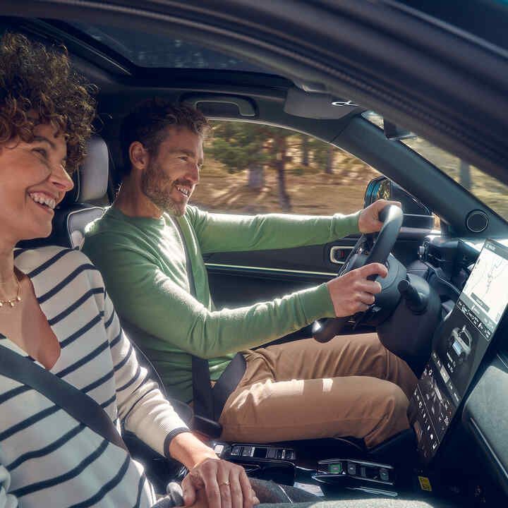 Pareja conduciendo el Honda e:Ny1 en el campo. 