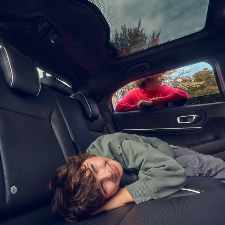 Niño acostado en el asiento trasero con la madre parada en la ventana del Honda e:Ny1.