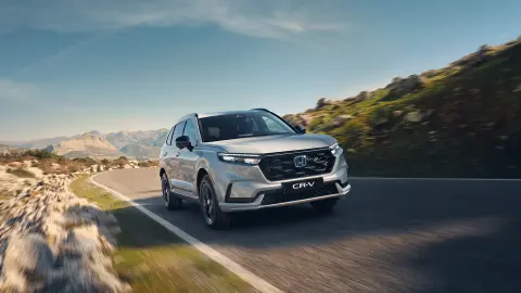 Coche híbrido CR-V Plugin blanco circulando por la carretera en una zona de montaña.