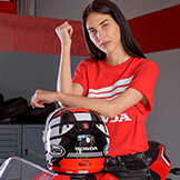 Señora vistiendo un top rojo de Honda apoyada en un casco de motocicleta Honda.