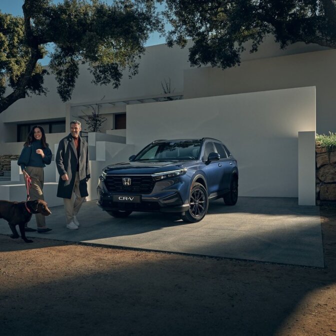 Una pareja paseando a un perro junto a un Honda CR-V estacionado.