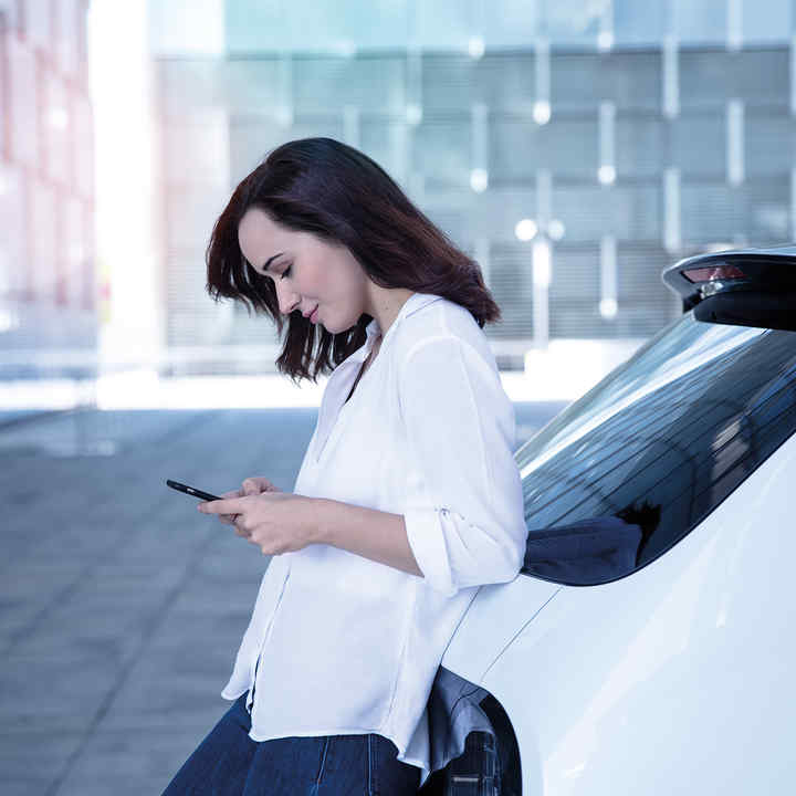 Señora apoyada en la parte trasera de un Honda e mirando el teléfono