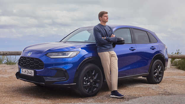 Max Verstappen apoyado en un ZR-V estacionado, mostrando la estética deportiva del nuevo SUV híbrido de Honda.