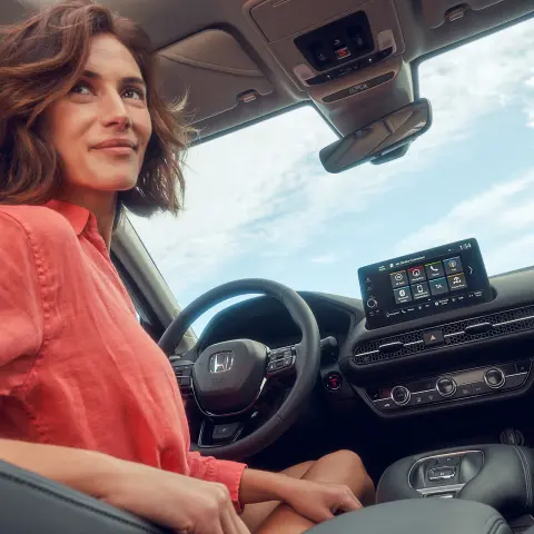 Mujer sentada en asiento del conductor usando la pantalla de información y entretenimiento del Honda ZR-V Híbrido.