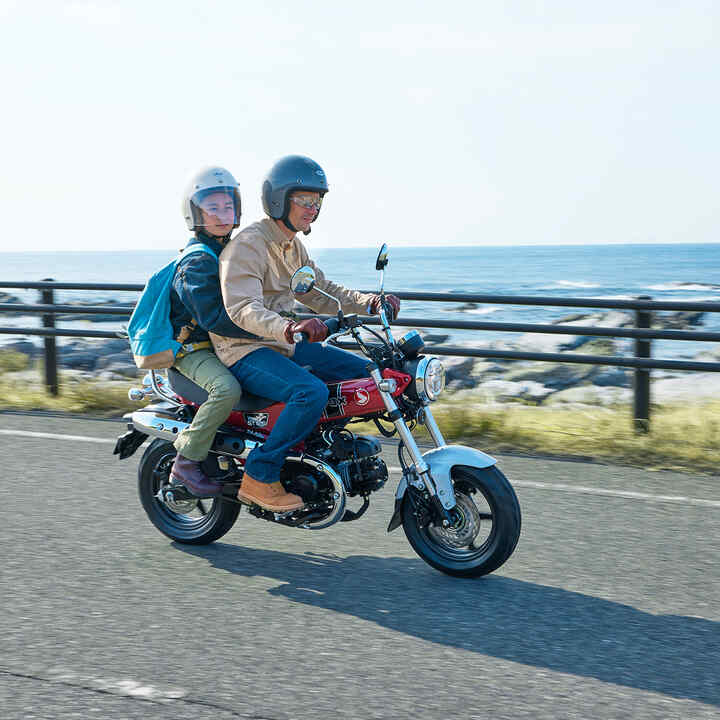 Honda Dax 125 en carretera costera con conductor y pasajero