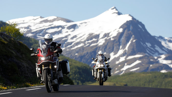 Dos motos recorren la carretera con las montañas nevadas a lo lejos.