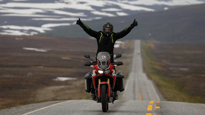 Hombre en una Honda Africa Twin con los brazos en alto en las carreteras de Nordkapp.