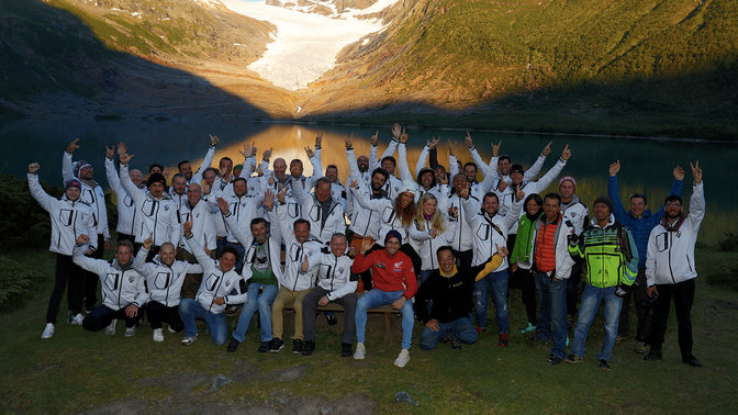 Participantes de la aventura Honda Adventure Roads de celebración a orillas del agua al atardecer.