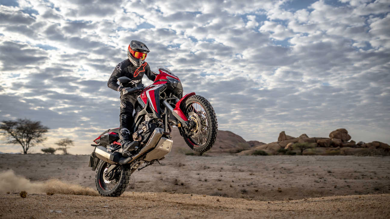 Honda Africa Twin, lateral delantero derecho de tres cuartos, haciendo un caballito en un paisaje desértico