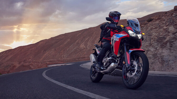 Modelo conduciendo una moto CRF1100L Africa Twin por una carretera de montaña.