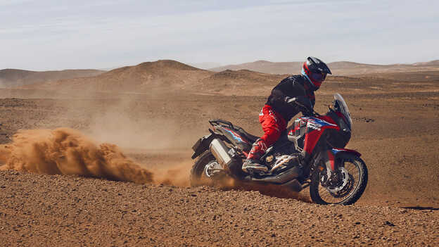 Modelo conduciendo una moto CRF1100L Africa Twin en lugar desértico.