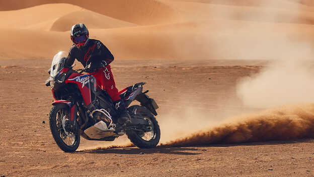 Modelo conduciendo una moto CRF1100L Africa Twin en lugar desértico.