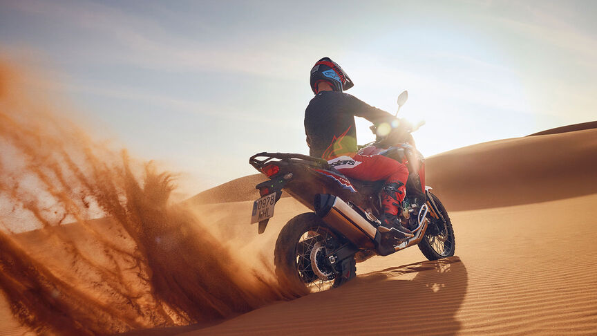 Modelo conduciendo una moto CRF1100L Africa Twin en lugar desértico.