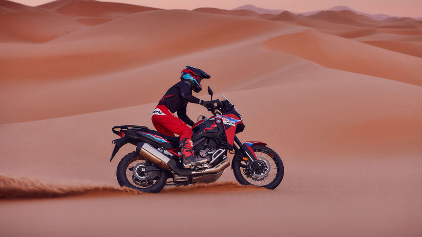 Modelo conduciendo una moto CRF1100L Africa Twin en lugar desértico.