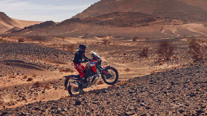 Modelo conduciendo una moto CRF1100L Africa Twin en lugar desértico.