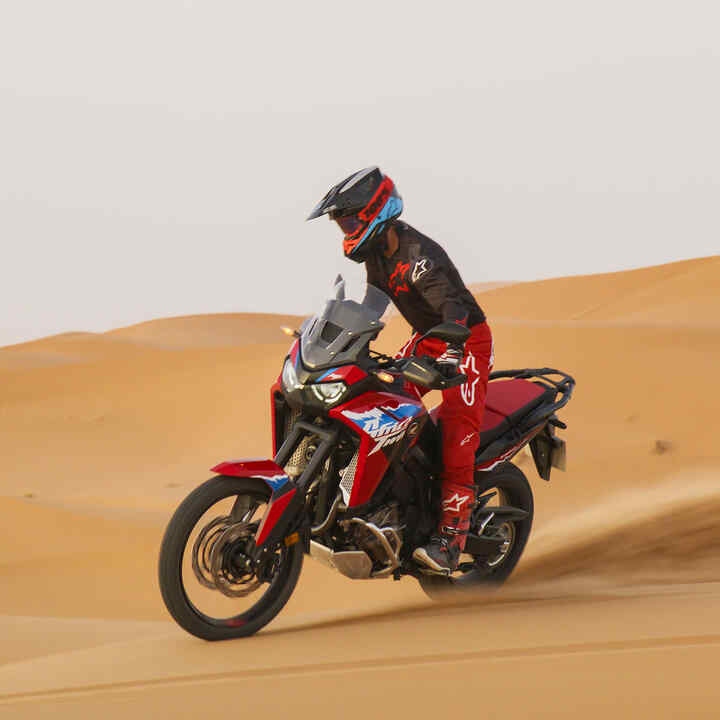 Modelo conduciendo una moto CRF1100L Africa Twin en una carretera por un lugar desértico.