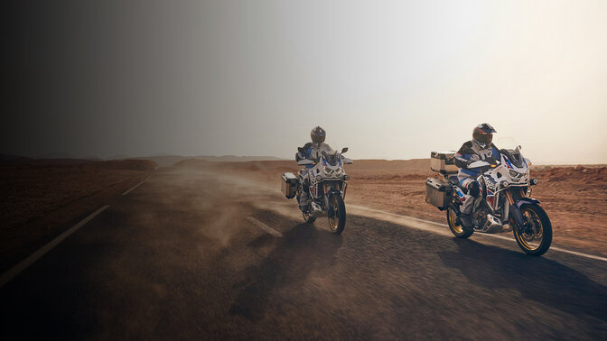 Vista frontal de 3/4 de conductores en CRF1100 Africa Twin Adventure Sports en carretera del desierto. 