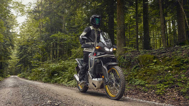 Modelo conduciendo una Honda XL750 Transalp en una zona forestal.