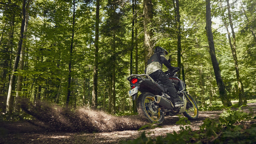 Modelo circulando con la motocicleta XL750 Transalp en una zona boscosa.