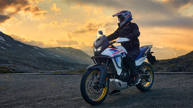 Modelo conduciendo una motocicleta XL750 Transalp en la carretera en un entorno montañoso.
