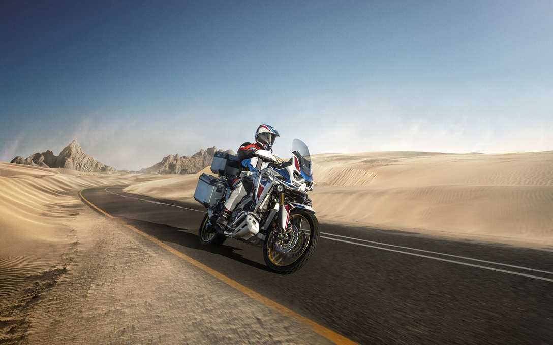 Honda Africa Twin Adventure Sports, lateral delantero derecho de tres cuartos, conduciendo por carretera a través de un paisaje desértico