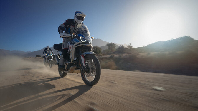 Dos pilotos del Honda Adventure Roads fuera de la carretera con montañas al fondo