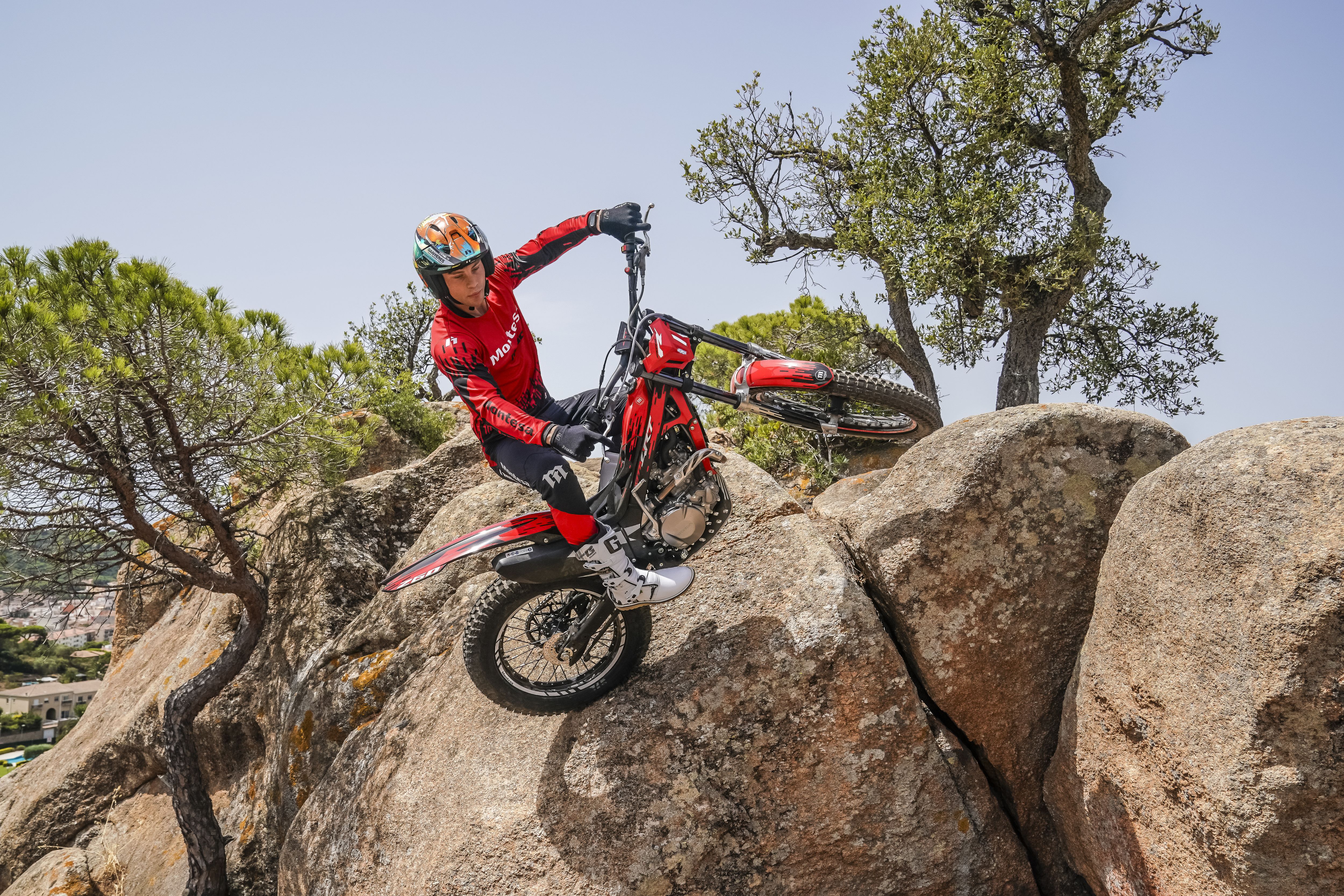 Un conductor maniobra con una motocicleta Montesa Cota 4RT 260R roja por encima de rocas empinadas en un día soleado.