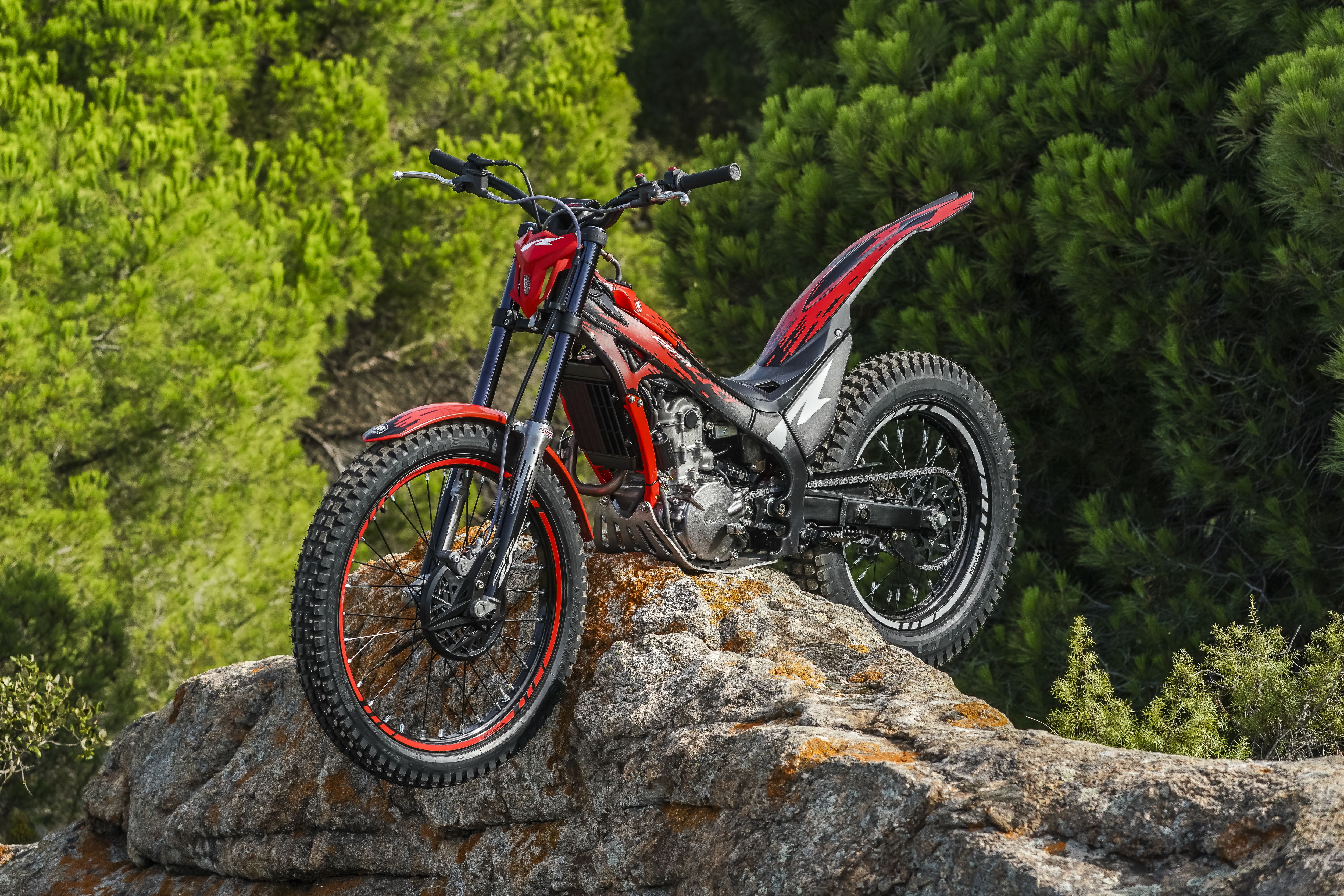 Motocicleta de trial Montesa Cota 260R encima de una cornisa rocosa en un entorno boscoso.
