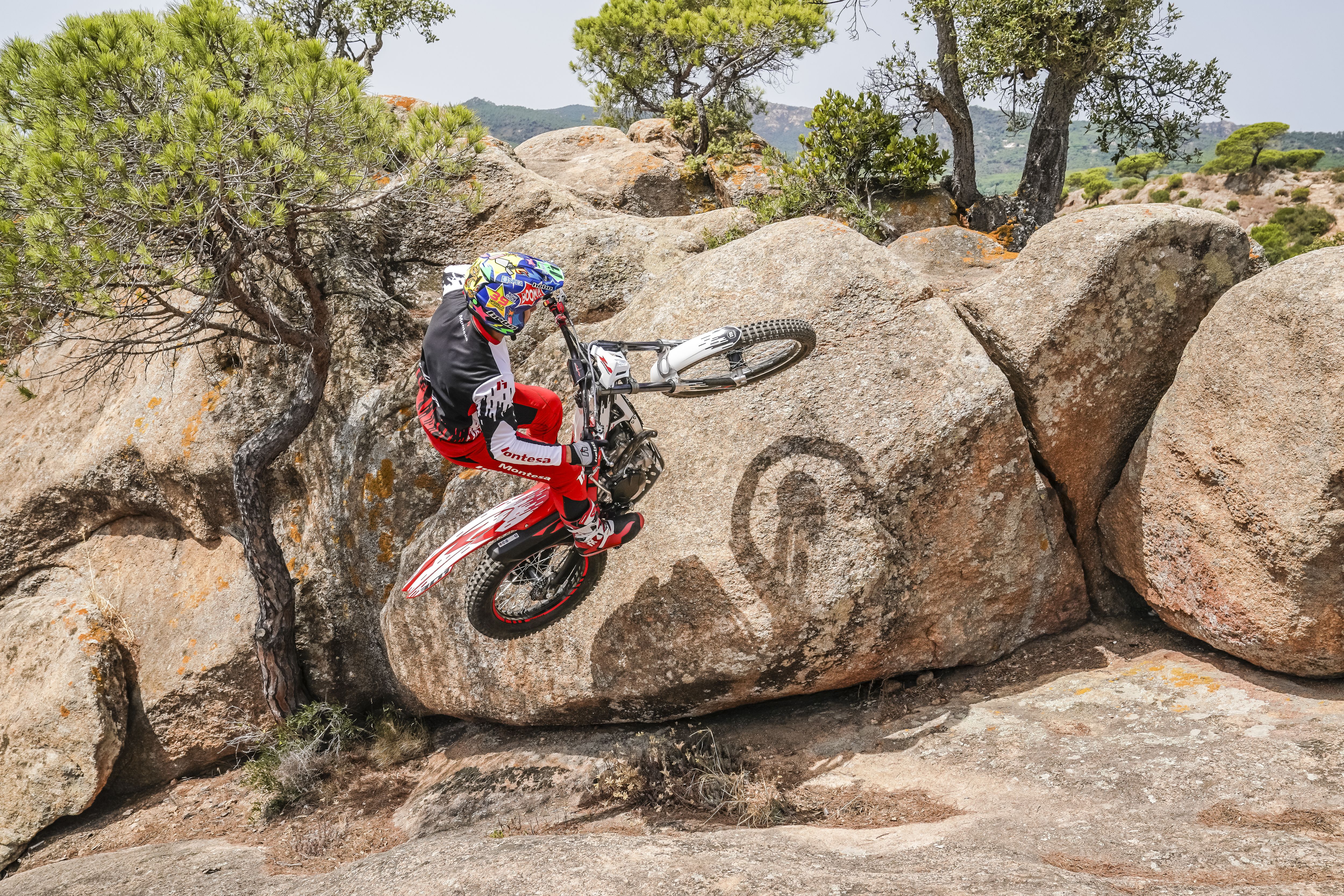 Conductor de motocicleta haciendo un caballito con una Montesa Cota 301RR encima de una formación rocosa.