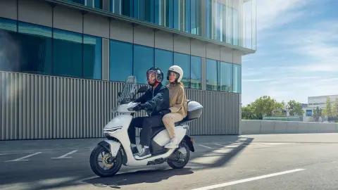 Modelos conduciendo la motocicleta Honda CUV e en un entorno urbano.