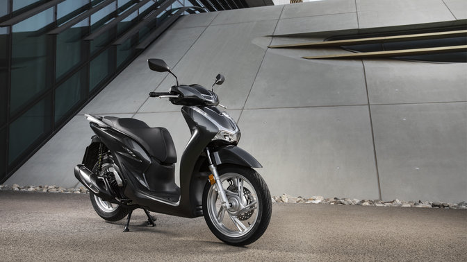 Honda Sh125i con topbox y parabrisas en la calle.