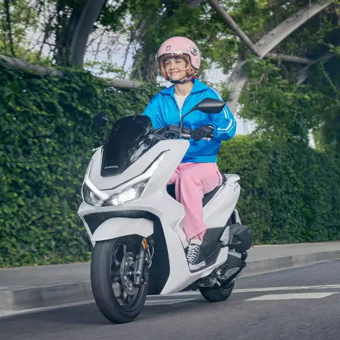 Modelo conduciendo una motocicleta PCX125 en un entorno urbano.