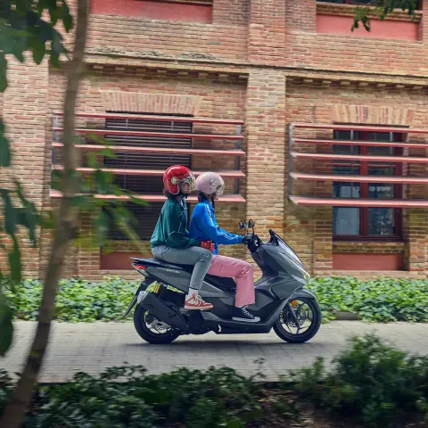 Vista lateral de modelos conduciendo la motocicleta PCX125 en un entorno de ciudad.