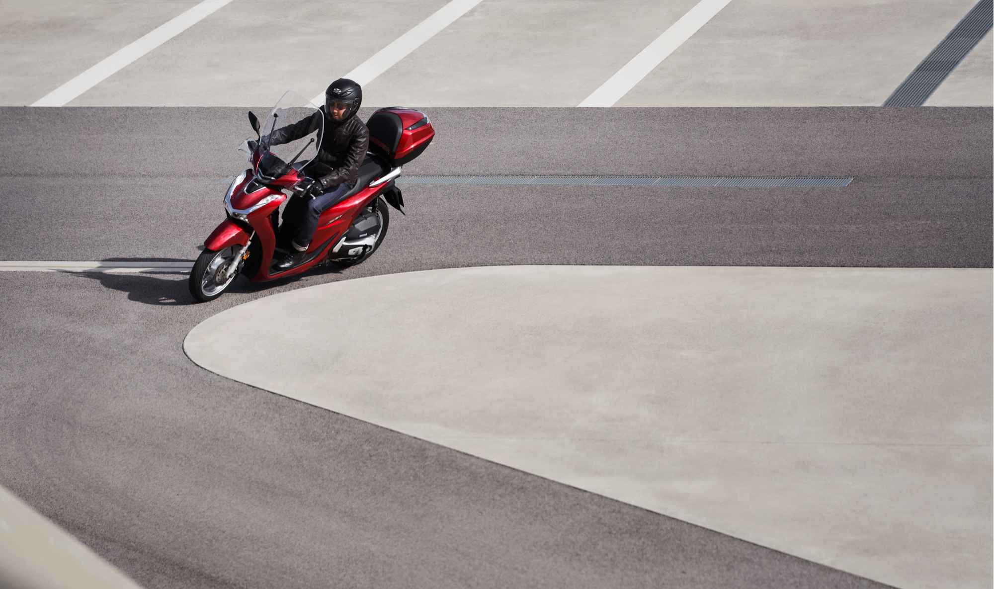 Honda-SH125i, vista frontal de tres cuartos del lateral izquierdo, con conductor, giro a la izquierda en carretera