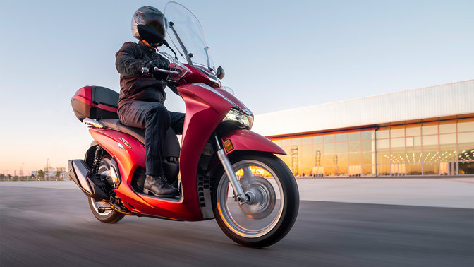 Honda SH350i, vista delantera derecha de tres cuartos, con conductor, en carretera, moto roja