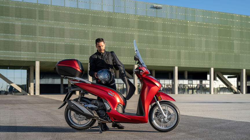 Honda SH350i, vista delantera derecha de tres cuartos, con conductor, en carretera, moto roja