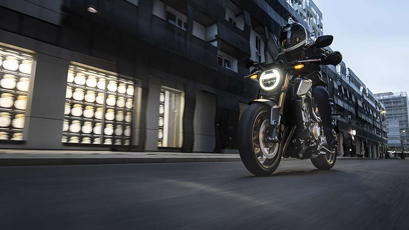 CB650R Neo Sports Café, lateral izquierdo de tres cuartos con piloto, en un paisaje urbano