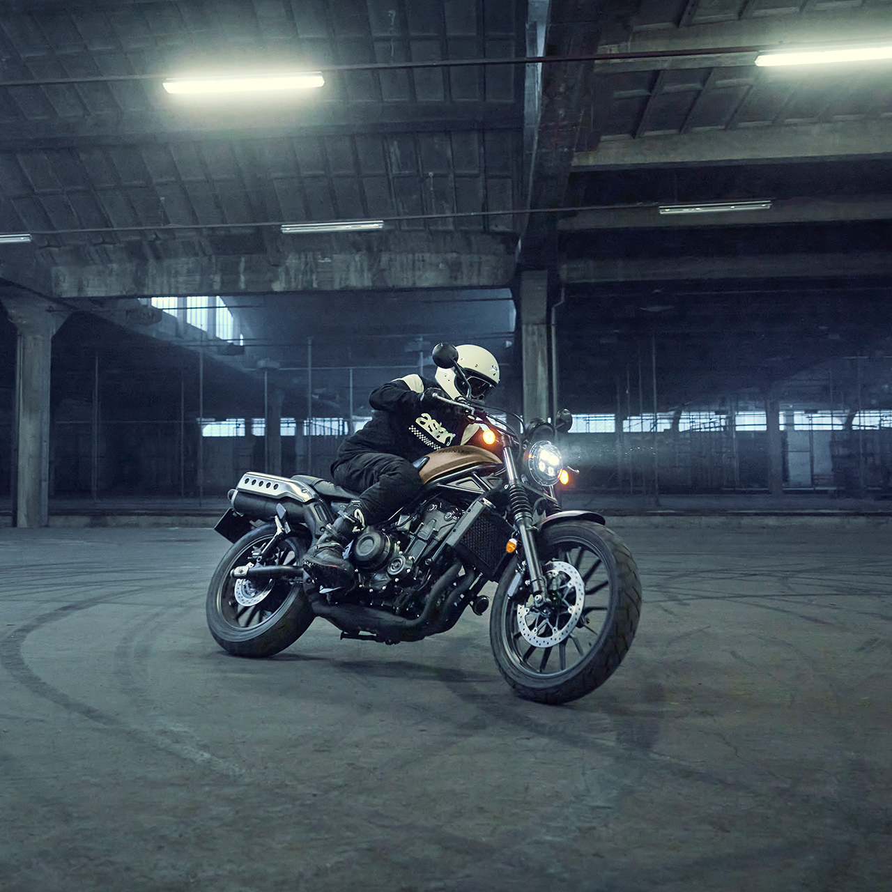 Modelo conduciendo una motocicleta Honda CL500 en un estacionamiento.