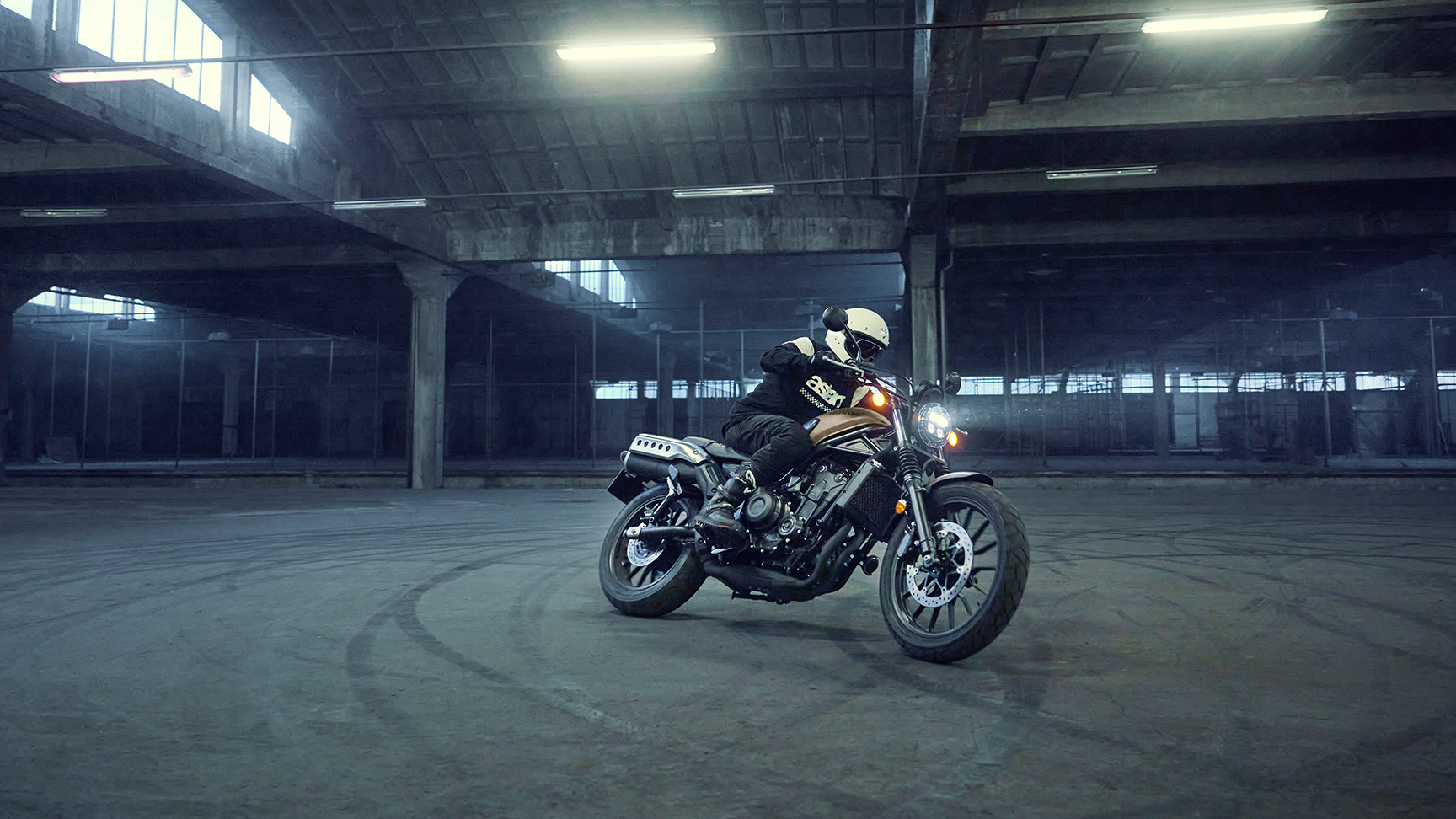 Modelo conduciendo una motocicleta Honda CL500 en un estacionamiento.