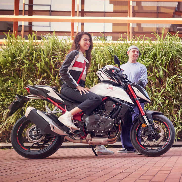 Conductor femenino en Honda CB750 Hornet con hombre bailando.