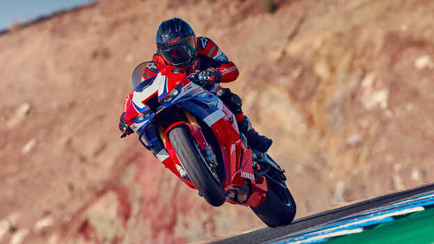 Piloto con Honda CBR1000rr-r Fireblade en la pista con la rueda delantera elevada.