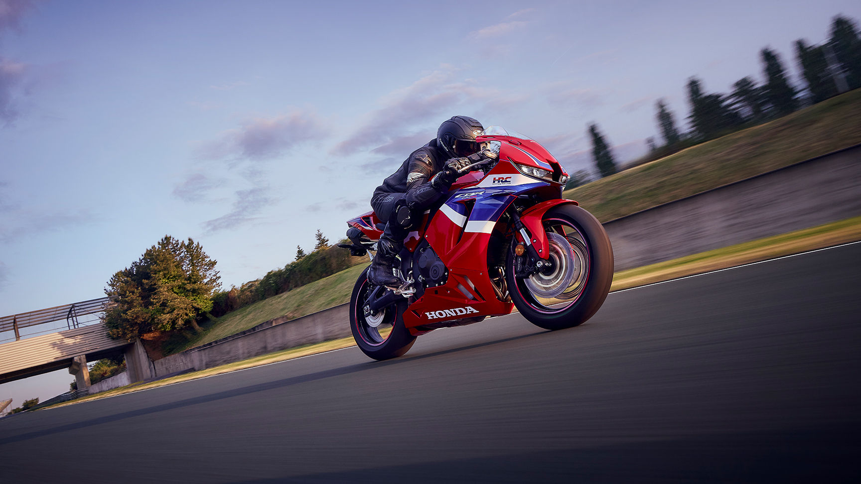 CBR600RR en pista con el piloto en una curva al atardecer.
